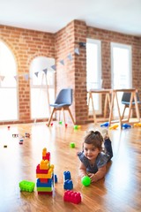 Beautiful toddler lying down on the floor playing with building blocks toys at kindergarten