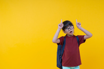 Young Asian Thai girl student in red shirt with shoulder bag pointing up on yellow background in studio