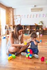 Young beautiful teacher and toddler playing with building blocks toy at kindergarten