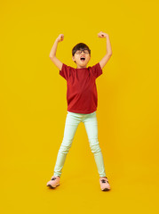 Young girl in red shirt celebrate and raised hands up to success on yellow background in studio