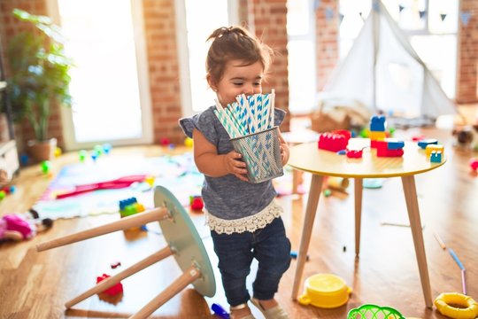 Beautiful toddler holding glass of striped straws standing at kindergarten