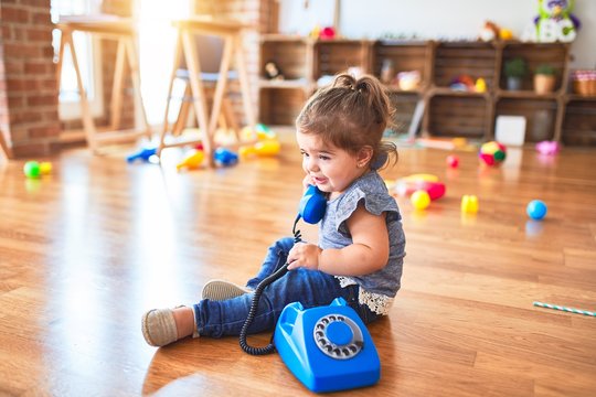 Beautiful toddler sitting on the floor playing with vintage phone at kindergarten