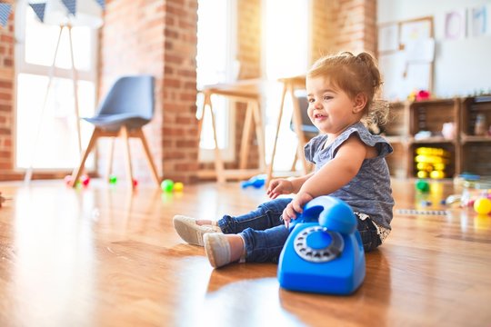 Beautiful toddler sitting on the floor playing with vintage phone at kindergarten