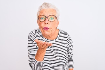 Senior grey-haired woman wearing striped navy t-shirt glasses over isolated white background looking at the camera blowing a kiss with hand on air being lovely and sexy. Love expression.