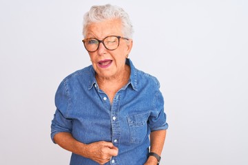 Senior grey-haired woman wearing denim shirt and glasses over isolated white background winking...