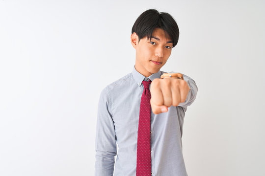Chinese businessman wearing elegant tie standing over isolated white background Punching fist to fight, aggressive and angry attack, threat and violence