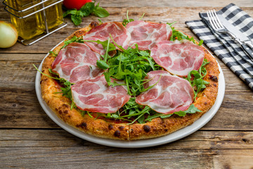 Pizza with Parma ham and arugula on wooden table