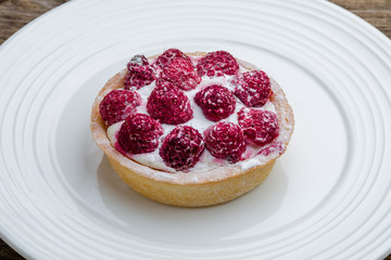 raspberry tartlet on a plate on wooden table