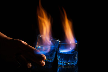 Close up, macro. Two glasses with cocktails, on the surface of which a blue-orange flame quivers. A...