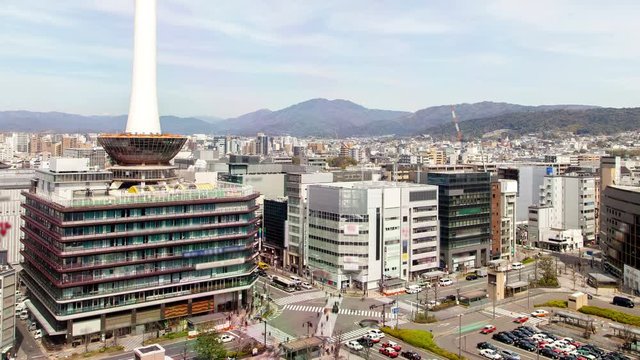 Timelapse zoom out Kyoto square with transport traffic on crossroad and TV tower among buildings by railway terminal against mountains on sunny day