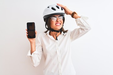 Young businesswoman wearing bike helmet holding smartphone over isolated white background stressed with hand on head, shocked with shame and surprise face, angry and frustrated. Fear and upset