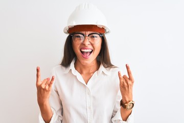 Young beautiful architect woman wearing helmet and glasses over isolated white background shouting with crazy expression doing rock symbol with hands up. Music star. Heavy concept.