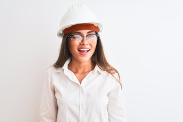 Young beautiful architect woman wearing helmet and glasses over isolated white background winking...