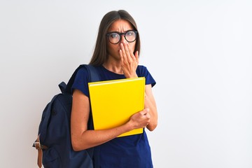 Young student woman wearing backpack glasses holding book over isolated white background cover mouth with hand shocked with shame for mistake, expression of fear, scared in silence, secret concept