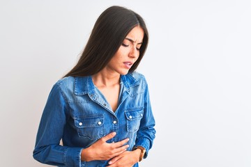 Naklejka premium Young beautiful woman wearing casual denim shirt standing over isolated white background with hand on stomach because indigestion, painful illness feeling unwell. Ache concept.