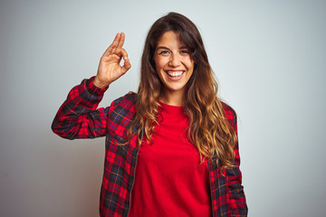 Young beautiful woman wearing red t-shirt and jacket standing over white isolated background smiling positive doing ok sign with hand and fingers. Successful expression.