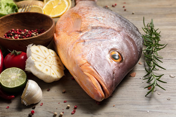 Fresh raw red snapper fish with spices, herbs and vegetables for cooking on wooden background.