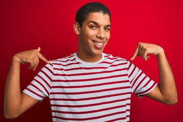 Young handsome arab man wearing striped t-shirt over isolated red background looking confident with smile on face, pointing oneself with fingers proud and happy.