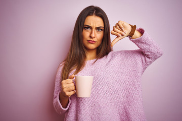 Young beautiful woman drinking cup of coffee standing over isolated pink background with angry...