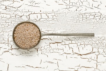 White whole, organic chia seeds heap in silver metal spoon on white rustic table background flat lay top view from above