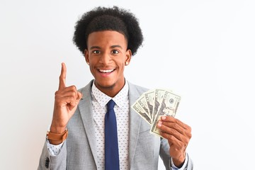 Young african american businessman holding dollars standing over isolated white background surprised with an idea or question pointing finger with happy face, number one