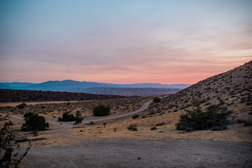 Pink desert sunset over remote desert road and blue mountains