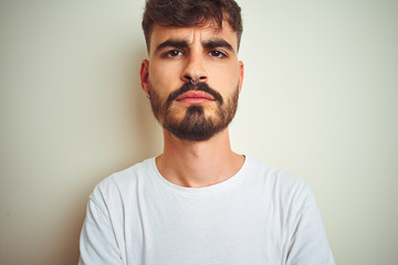 Obraz premium Young man with tattoo wearing t-shirt standing over isolated white background skeptic and nervous, disapproving expression on face with crossed arms. Negative person.