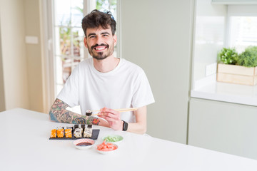 Young man eating asian sushi from home delivery with a happy face standing and smiling with a confident smile showing teeth