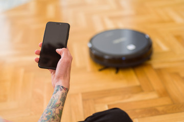 Close up of man hands controling automatic vacuum cleaner using electronic control of the mopping...
