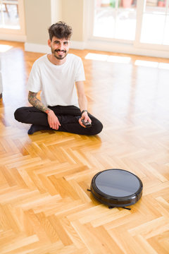 Young man using automatic vacuum cleaner to clean the floor, controling machine housework robot