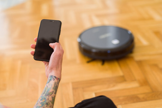 Close up of man hands controling automatic vacuum cleaner using electronic control of the mopping robot