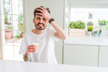 Young man drinking a coffee in a paper cup in the morning stressed with hand on head, shocked with shame and surprise face, angry and frustrated. Fear and upset for mistake.