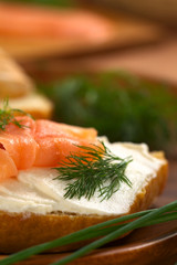 Canape of smoked salmon and cream cheese on wholewheat bun garnished with dill, chives on the side (Selective Focus, Focus on the front of the dill and on the front of the salmon on the left)