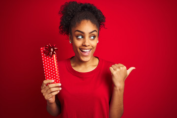 Young african american woman holding valentine gift over isolated red background pointing and...