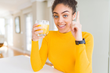 Young african american woman drinking a glass of fresh orange juice surprised with an idea or question pointing finger with happy face, number one