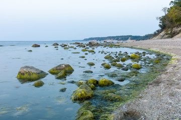 seascape with rocky beach covered with mud, large boulders in the water in the twilight