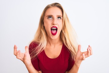 Young beautiful woman wearing red t-shirt standing over isolated white background crazy and mad shouting and yelling with aggressive expression and arms raised. Frustration concept.