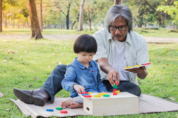 Daughter and grandfather playing toys in public garden sitting on a mat, they are happy and fun.