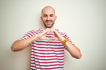 Naklejka premium Young bald man with beard wearing casual striped red t-shirt over white isolated background smiling in love doing heart symbol shape with hands. Romantic concept.