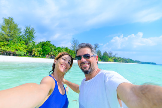 Happy man and woman taking selfie in tropical caribbean sea. Adult mid age traveling couple, real people having fun in vacation.