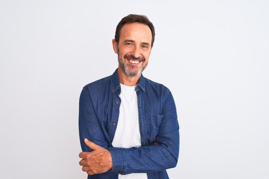 Middle age handsome man wearing blue denim shirt standing over isolated white background happy face smiling with crossed arms looking at the camera. Positive person.