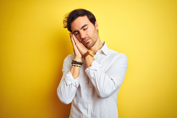 Young handsome businessman wearing elegant shirt standing over isolated yellow background sleeping tired dreaming and posing with hands together while smiling with closed eyes.