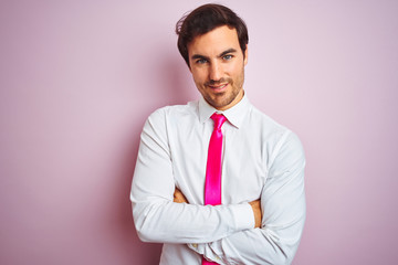 Young handsome businessman wearing shirt and tie standing over isolated pink background happy face smiling with crossed arms looking at the camera. Positive person.