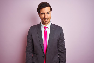 Young handsome businessman wearing suit and tie standing over isolated pink background winking...