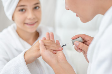 Young woman and his daughter are doing manicures at home. Mom and child girl are in bathrobes and...