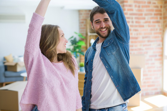 Young couple dancing celebrating moving to new apartment around cardboard boxes