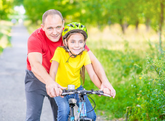 Happy family. Father teaches his daughter to ride a bicycle in the summer park