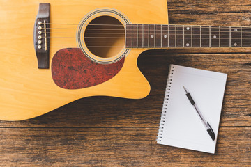 Top view of Acoustic guitar , Notebook paper and pen on wood background  and copy space