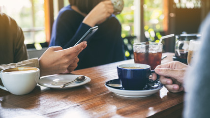 Closeup image of people using mobile phone and drinking coffee together in cafe