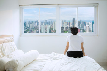 Woman looks at city scenery in apartment window